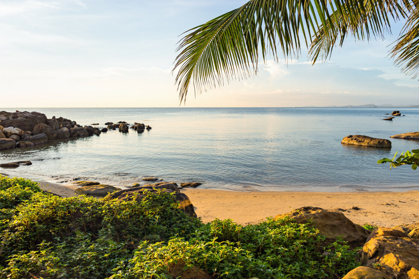 Scenic seascape with palm leaf, sand and stones at sunset on Long Beach of Phu Quoc island in Vietnam