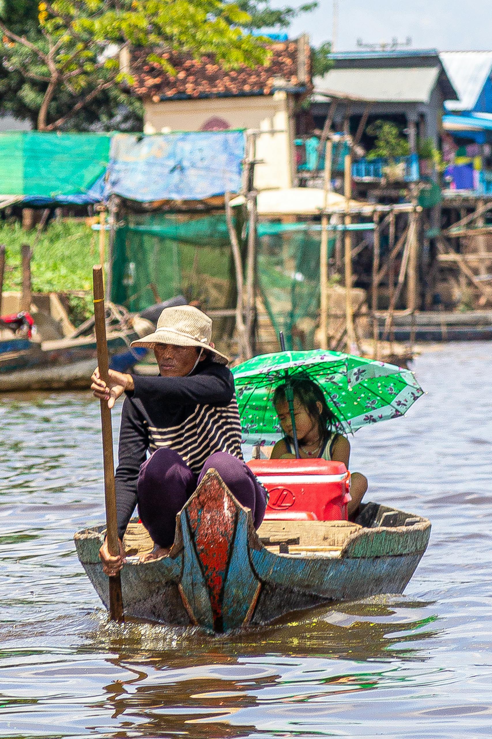 A Cambodian woman and child paddle through Tonle Sap River, showcasing local transportation.