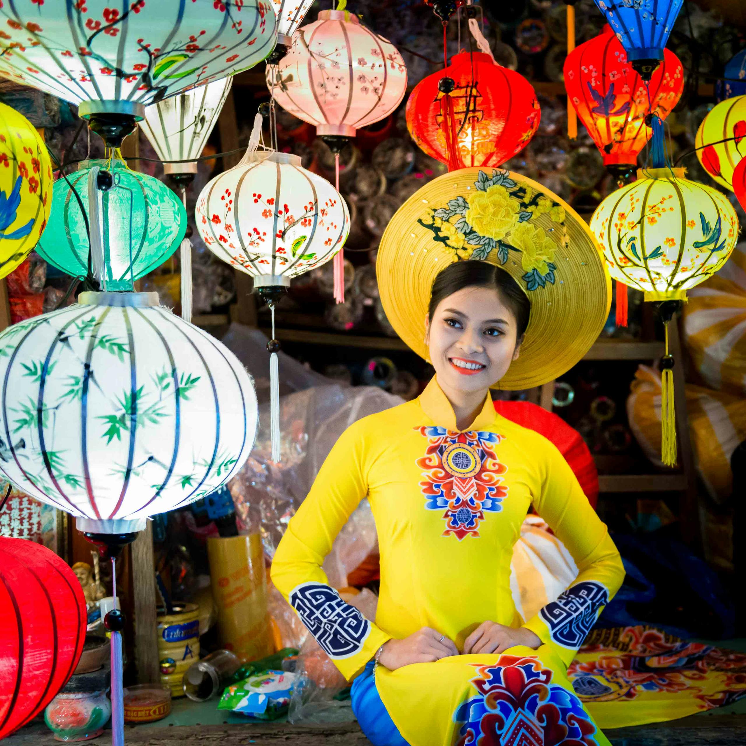 A Vietnamese woman in traditional attire smiles amid vibrant lanterns in Hoi An.