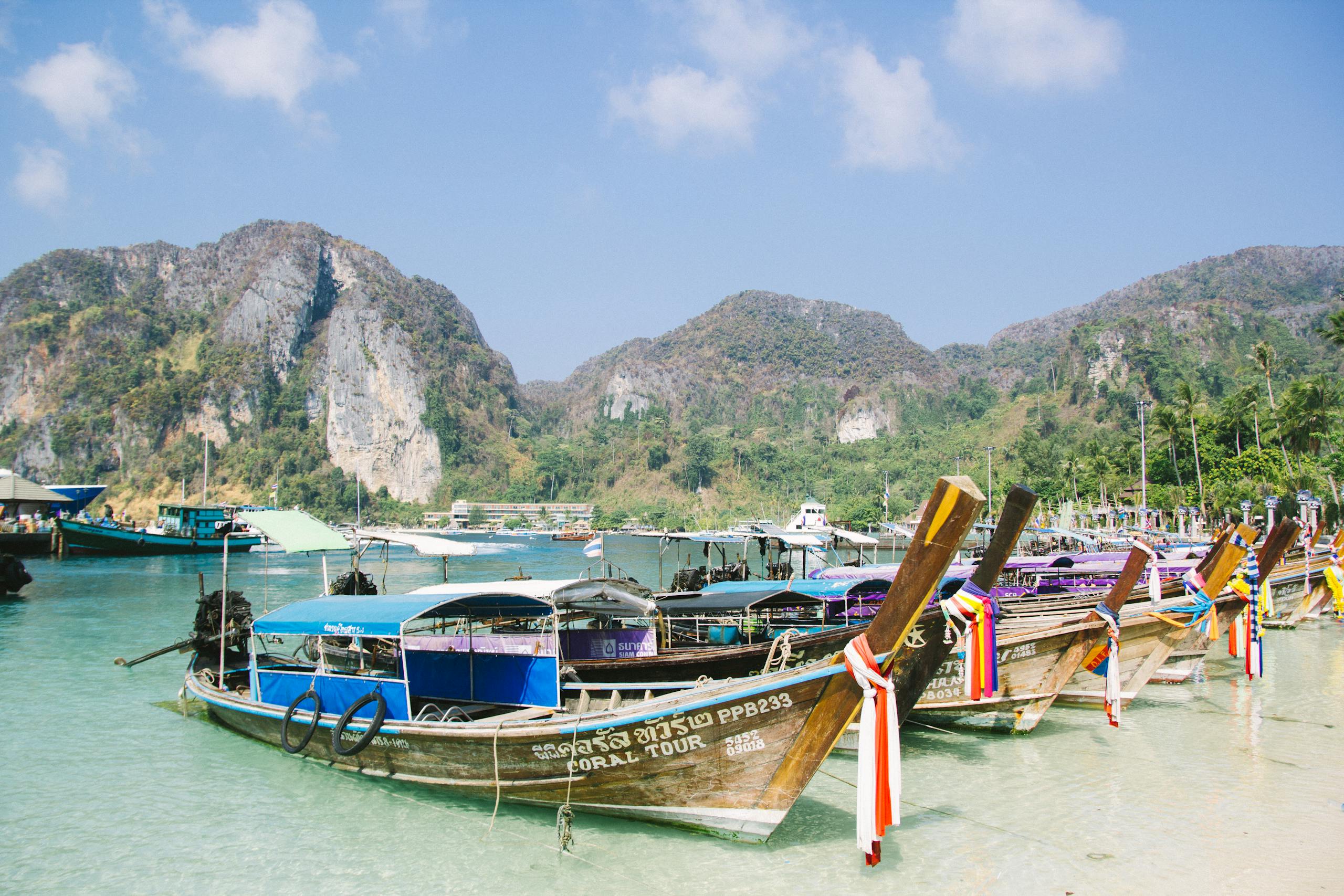 Colorful longtail boats docked by tropical mountains under a clear sky, perfect vacation scene.