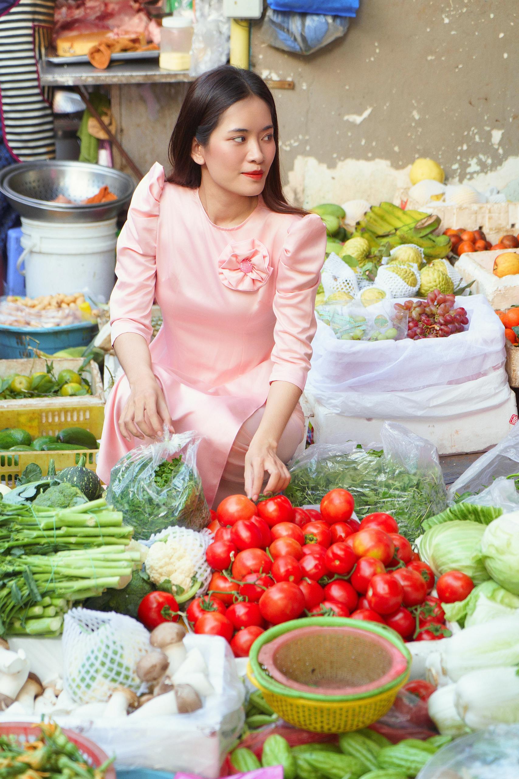 Colorful street market in Ho Chi Minh City with fresh produce and a woman in pink dress interacting.