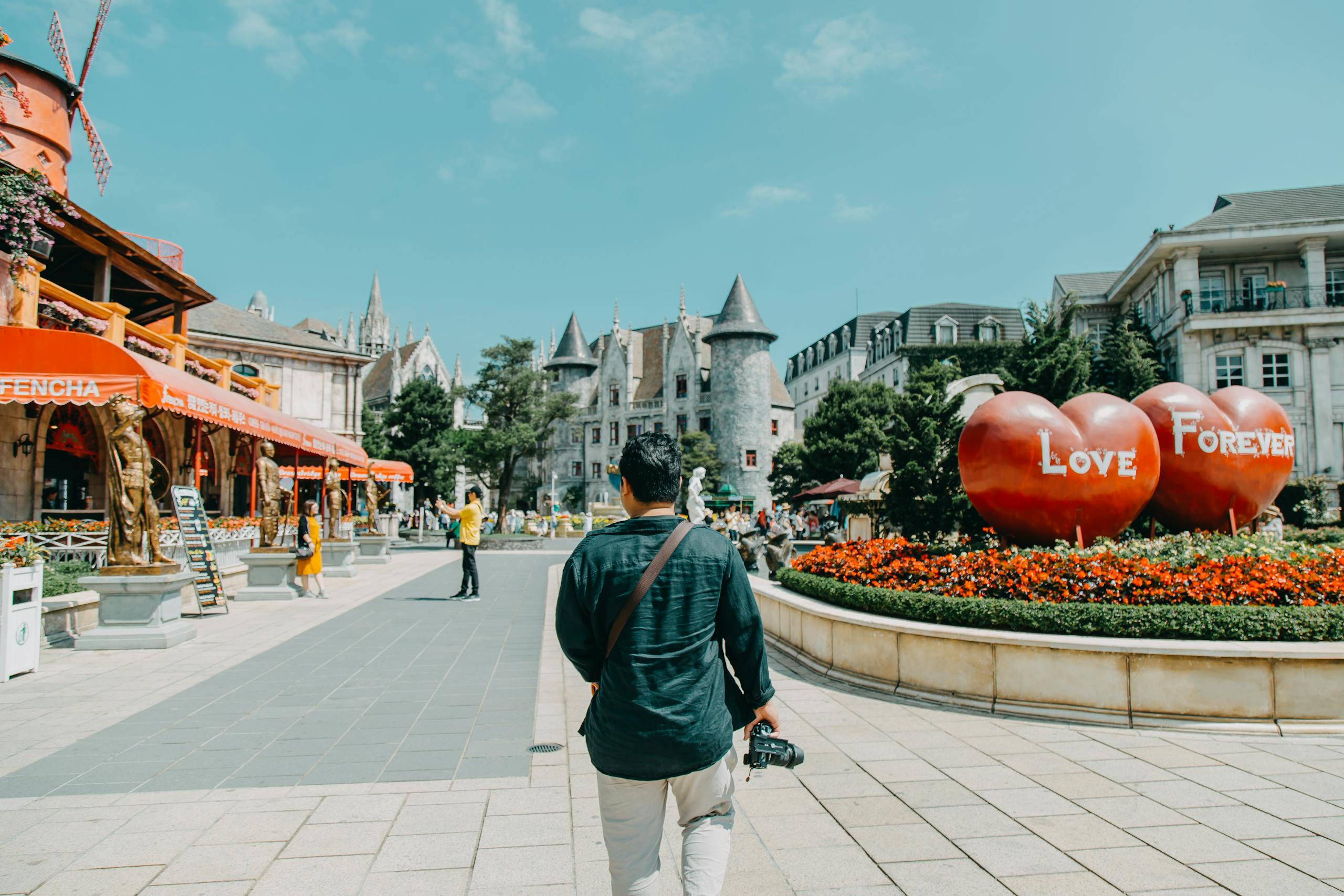 Man with camera walks in colorful urban plaza featuring bold architecture and 'Love Forever' display.