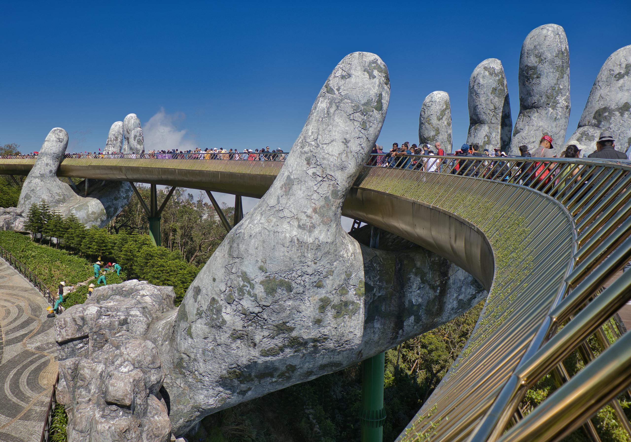 The iconic Golden Bridge with giant hand sculptures at Ba Na Hills, Vietnam, under a clear blue sky.