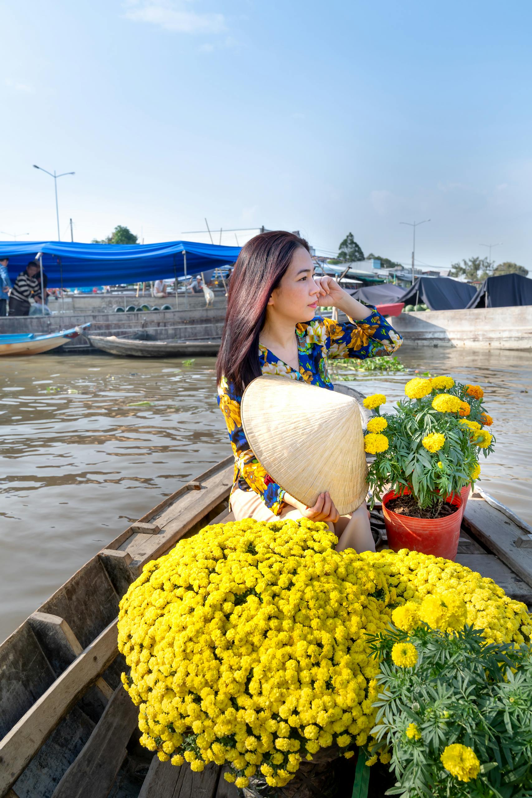 Woman with conical hat among flowers on a boat at a vibrant floating market.